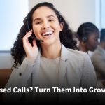 Smiling customer service representative with a headset assisting a caller in a professional office environment, with colleagues working in the background.